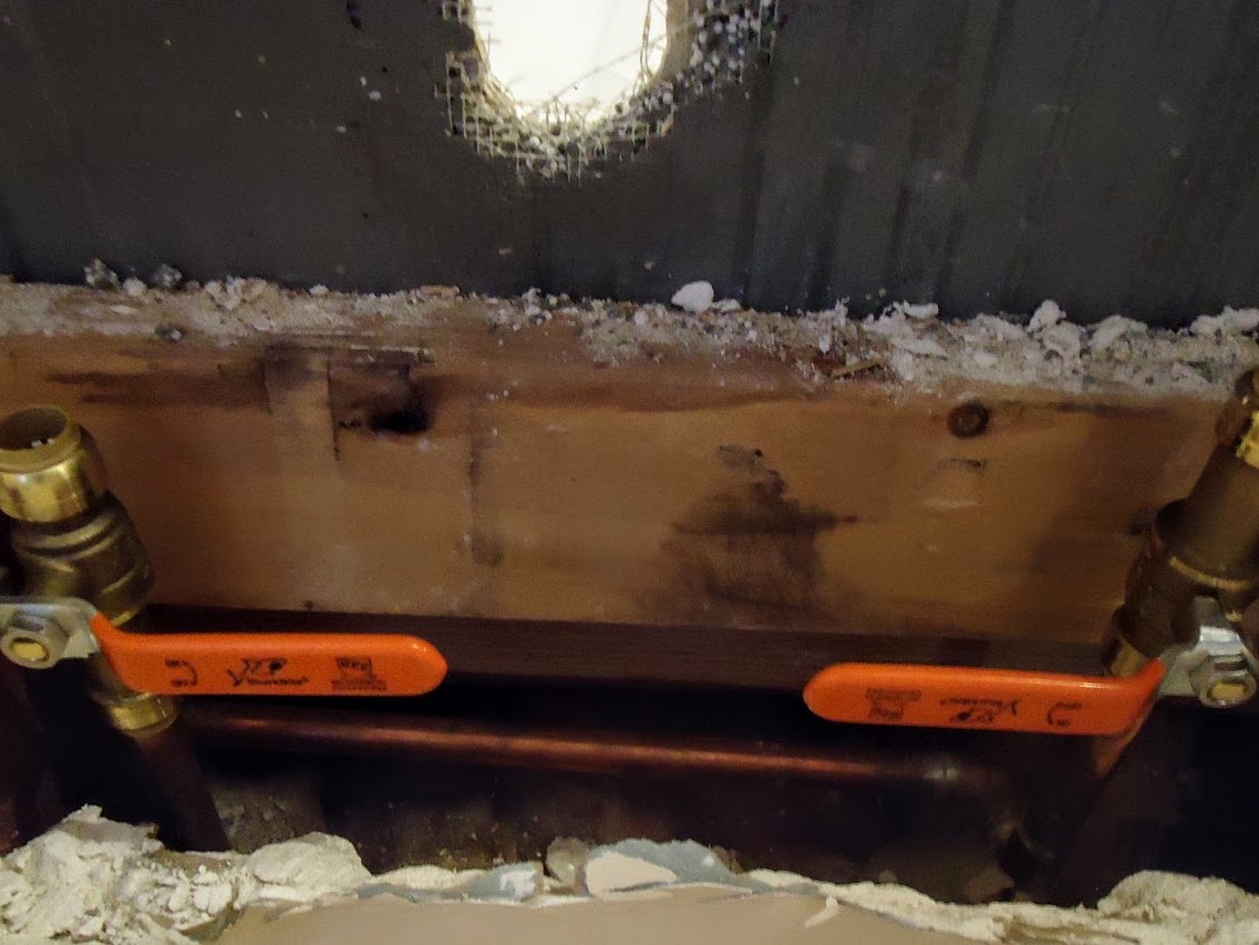 Two orange handled water shutoff valves on copper pipes inside a wall cavity