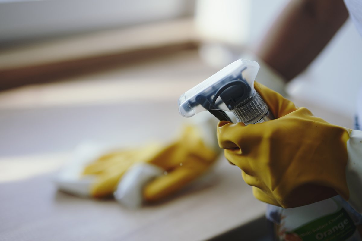 A gloved hand spraying disinfectant and wiping a surface clean