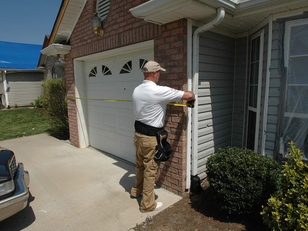 An inspector measuring a home exterior while documenting a loss for the claim file