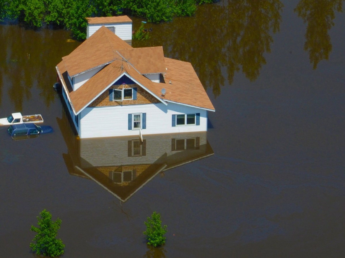 A house standing in deep floodwater after a river flood, the kind of loss that resets a restoration calendar