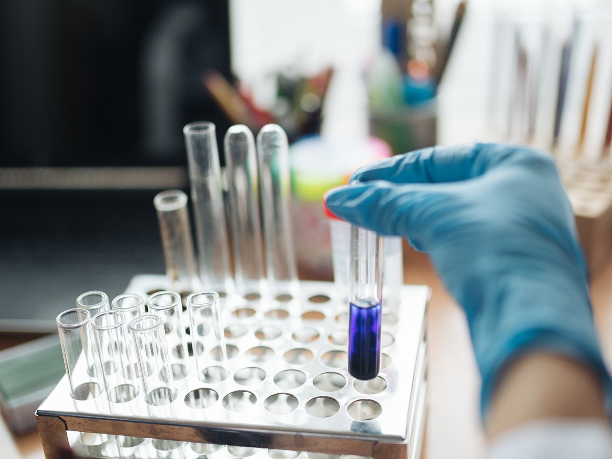 A gloved hand placing a sample tube into a laboratory rack during water testing