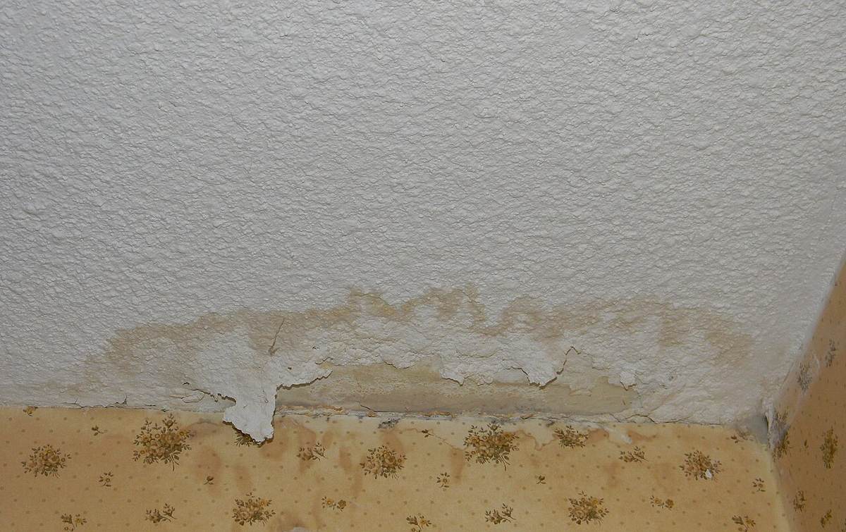 Water-stained ceiling and wall corner with peeling paint and bubbled plaster after an upstairs leak in a Tulsa home