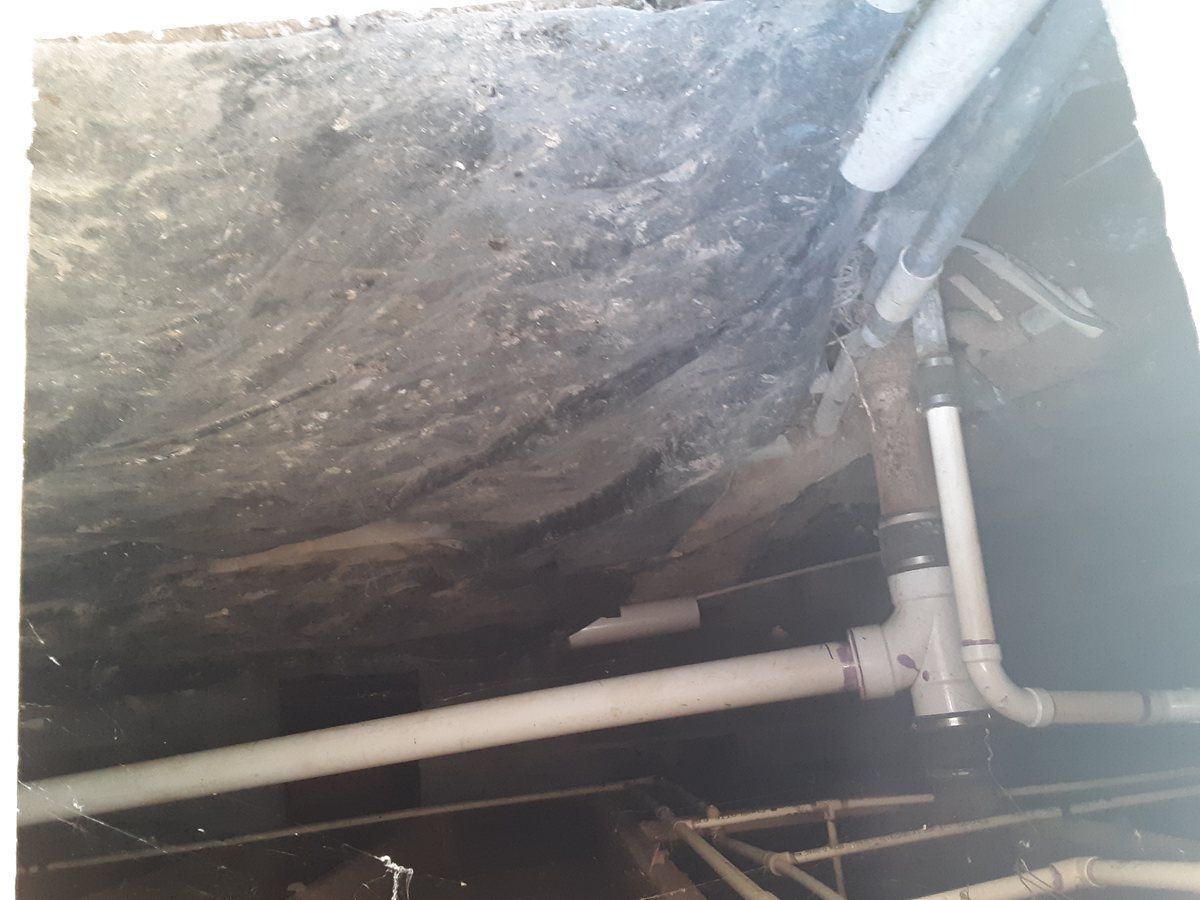 A dirt crawl space with plumbing pipes running overhead