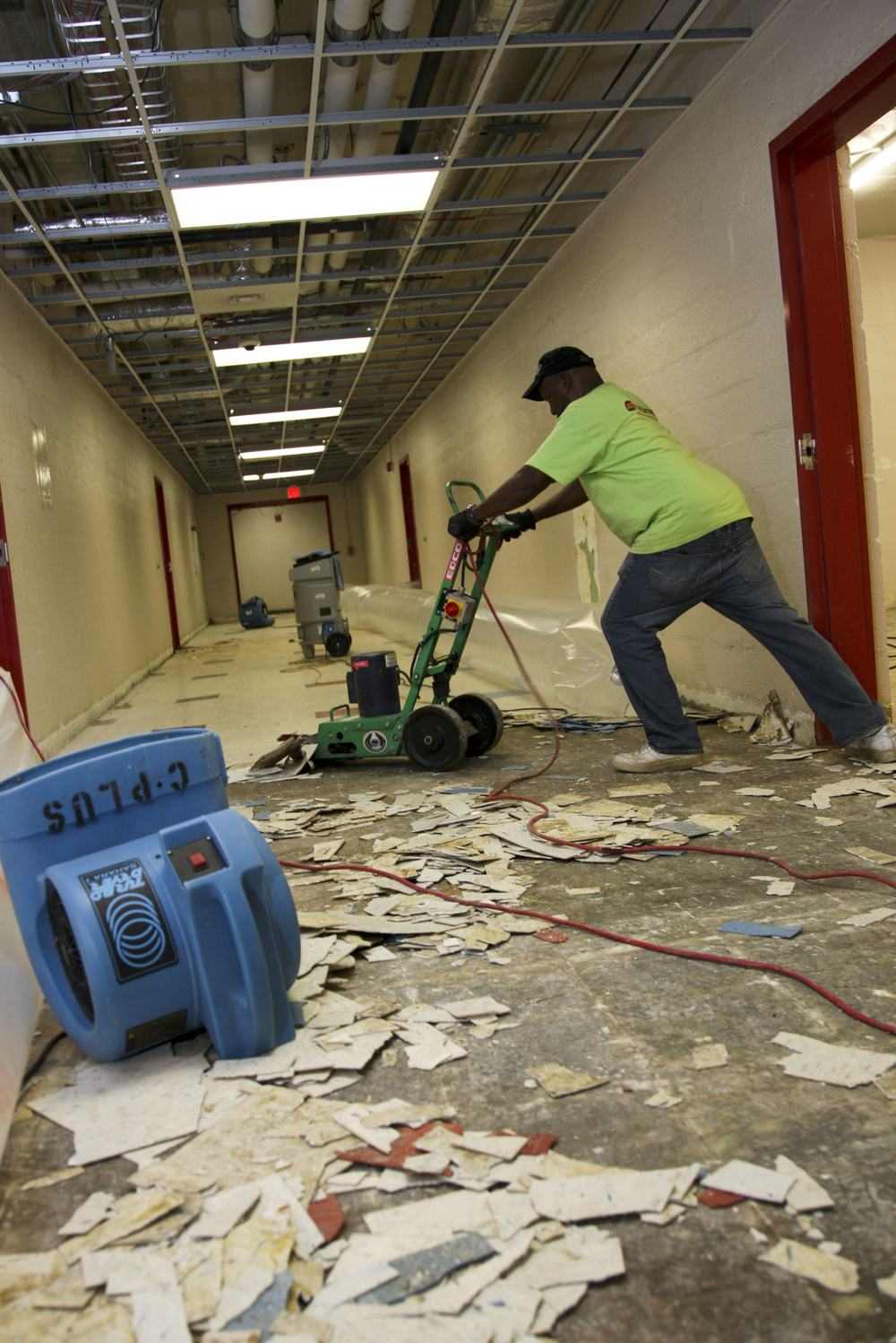 A worker removing damaged floor tiles during a flood cleanup, an air mover running nearby