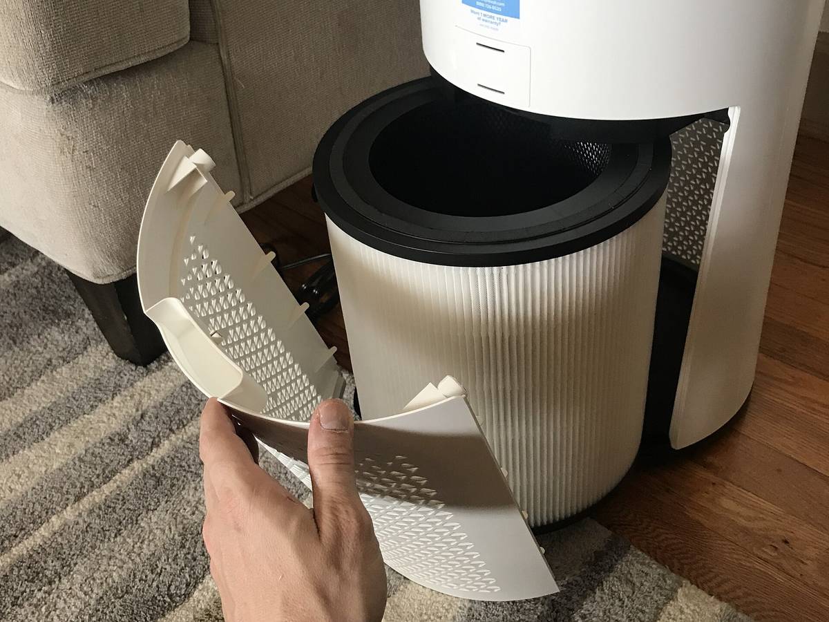 A homeowner opening a home air purifier to inspect the filter inside