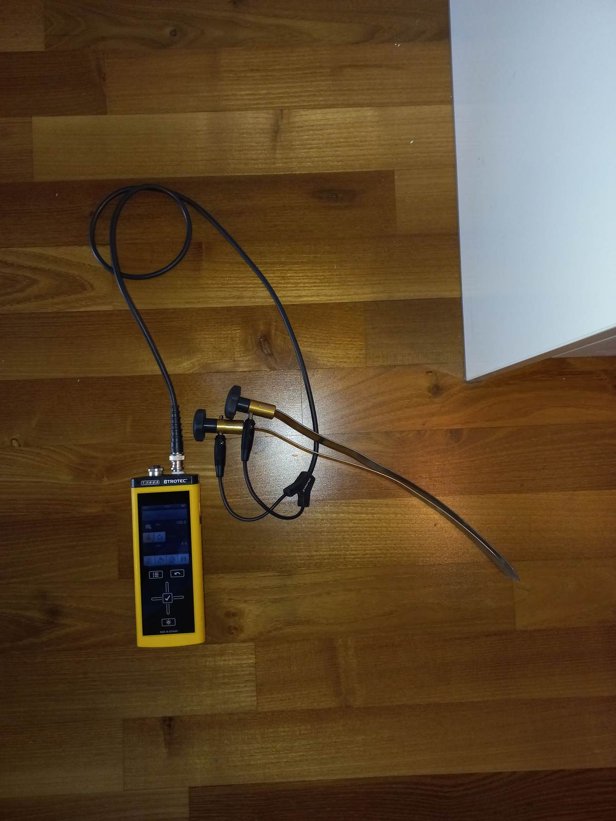 A moisture meter with probe leads taking readings on a hardwood floor