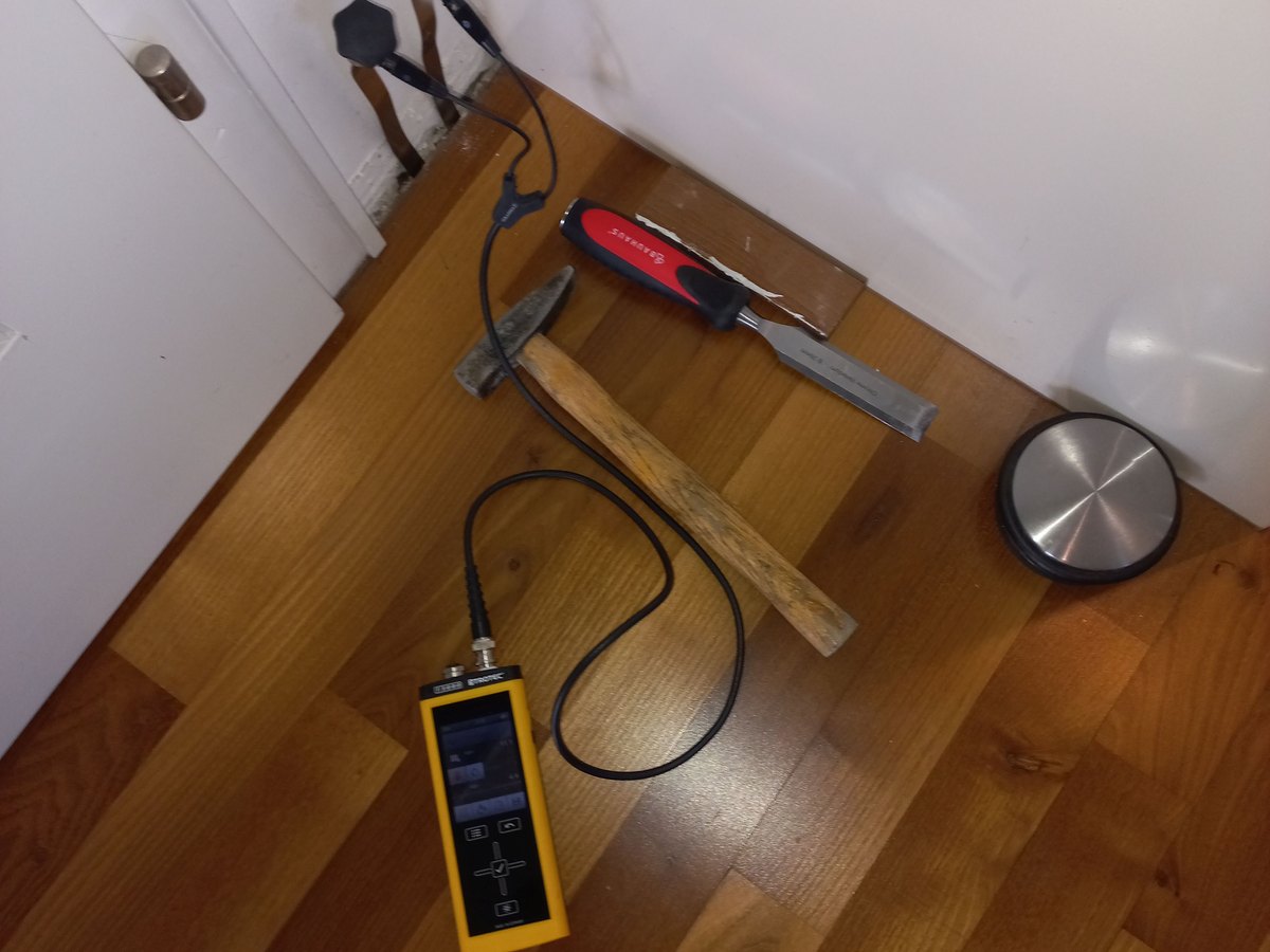 Moisture meter and probe setup measuring damp flooring in the corner of a room