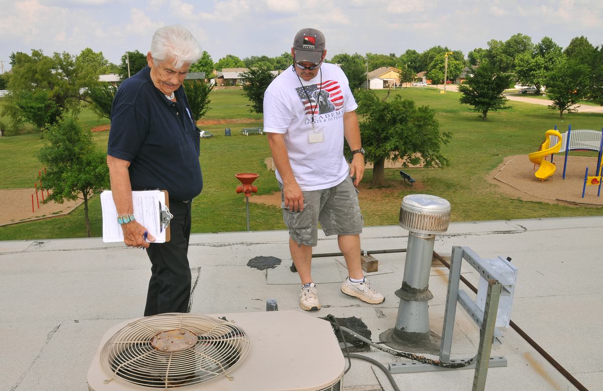 Two assessors with a clipboard inspecting a home roof for damage