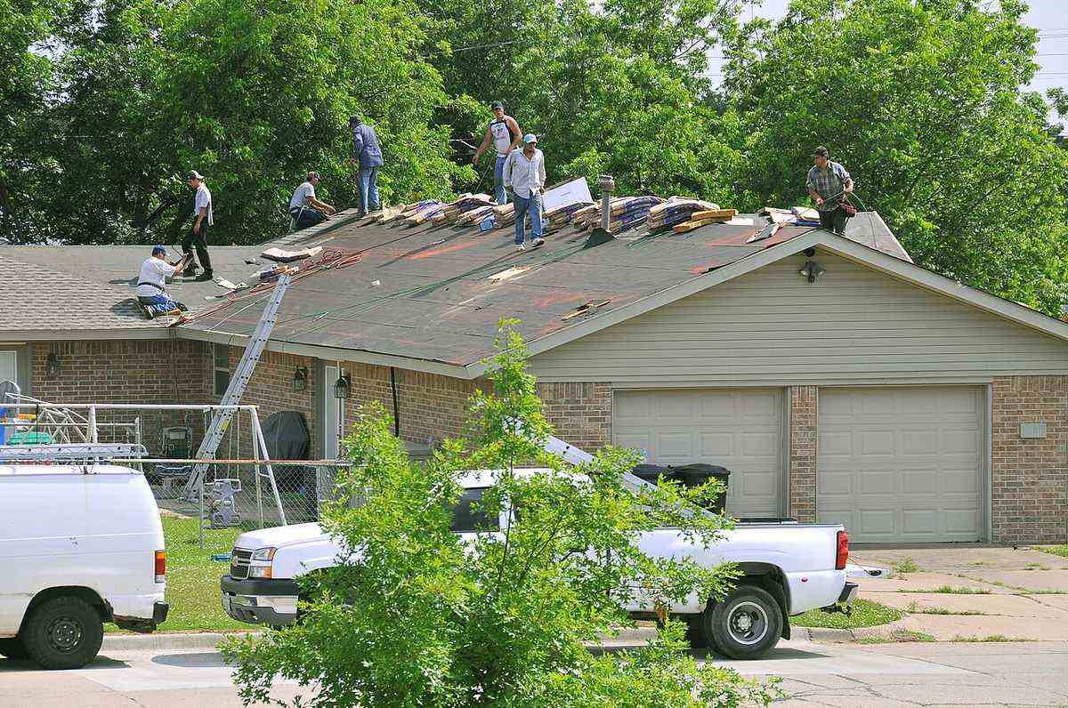 Roofing crew replacing storm-damaged shingles on a brick home, the repair that stops a roof leak at its source