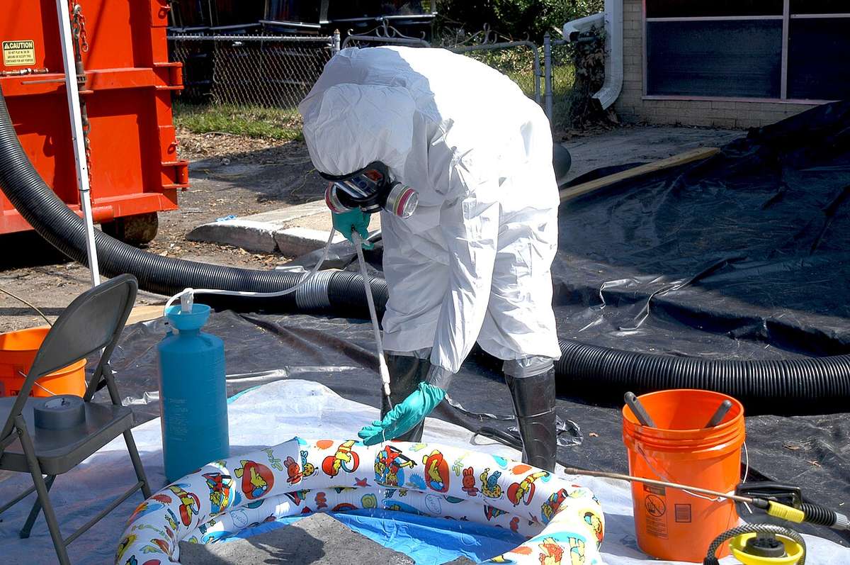 Cleanup technician in a full protective suit, gloves, and respirator during a decontamination job, the PPE protocol used on Tulsa sewage backups
