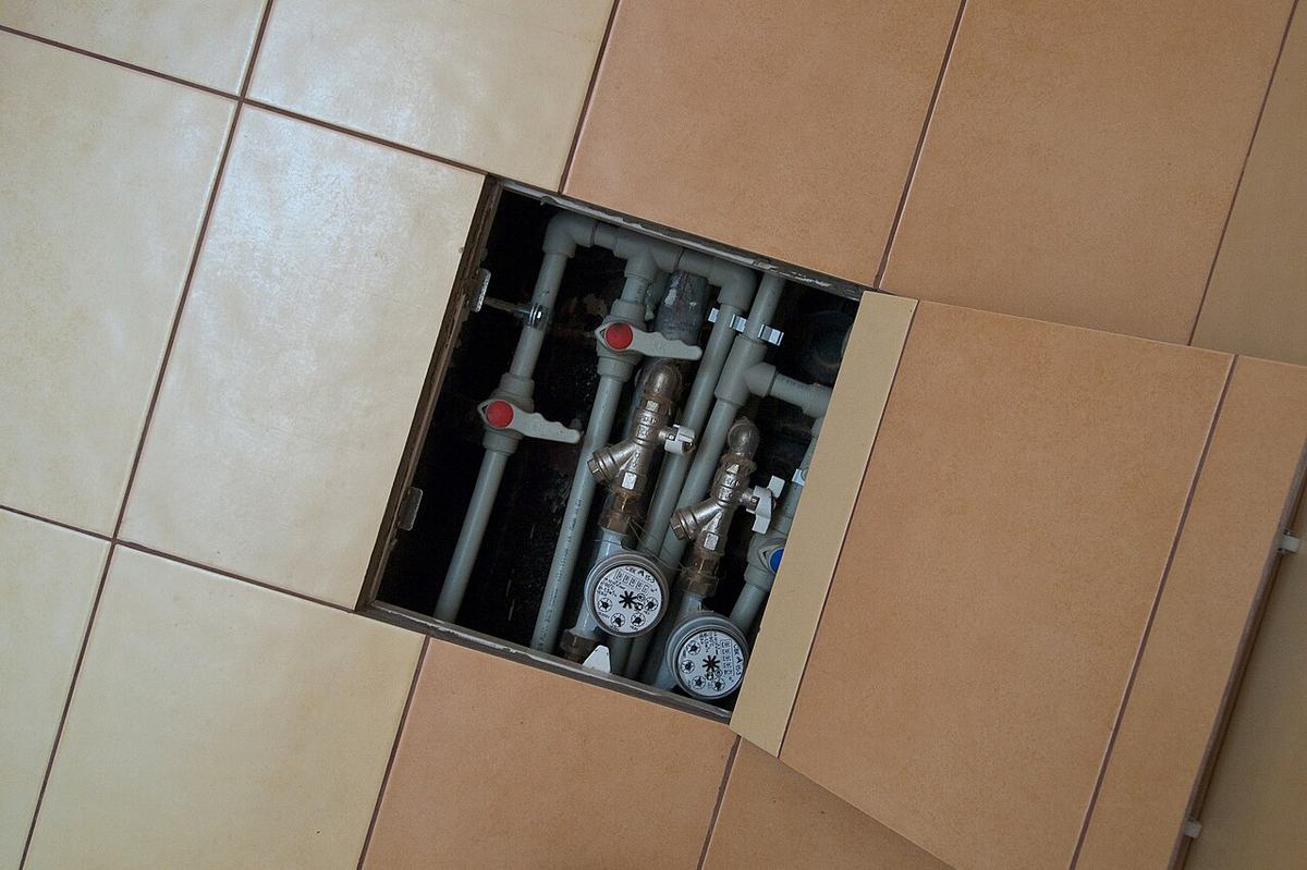 Plumbing lines and shutoff valves exposed through a floor access opening during a slab leak investigation in a Tulsa home