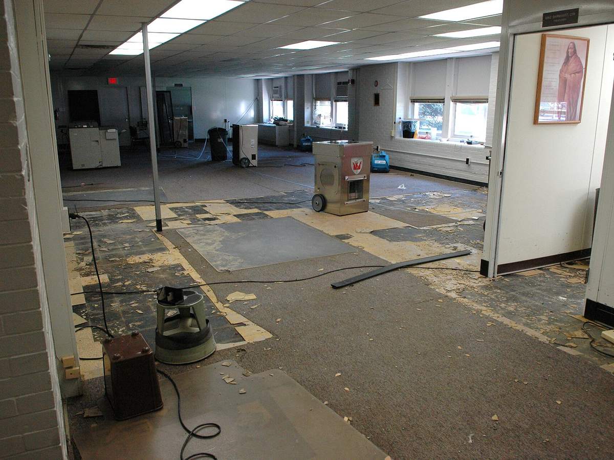 A large room with flooring removed and equipment running during structural drying