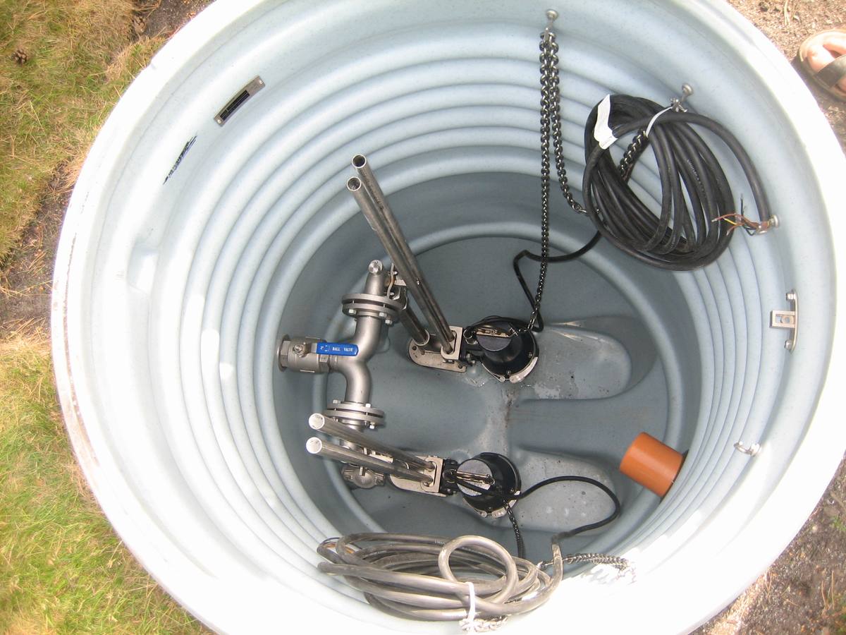 Looking down into a sump pit fitted with pumps, floats, and discharge piping