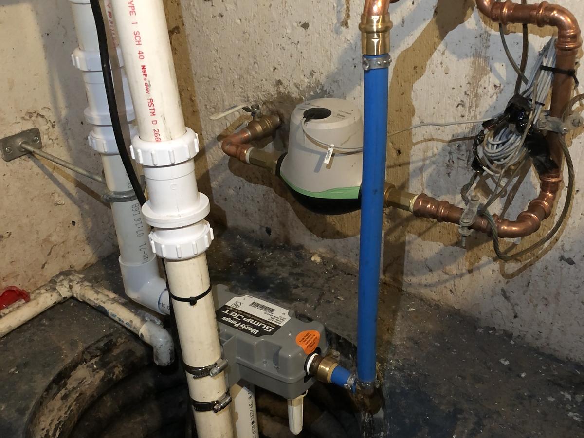 A sump pump and discharge piping installed in a basement utility corner