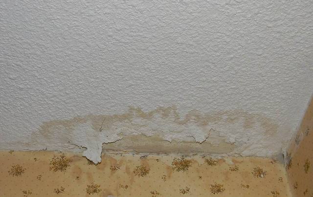 Water-stained ceiling and wall corner with peeling paint and bubbled plaster after an upstairs leak in a Tulsa home