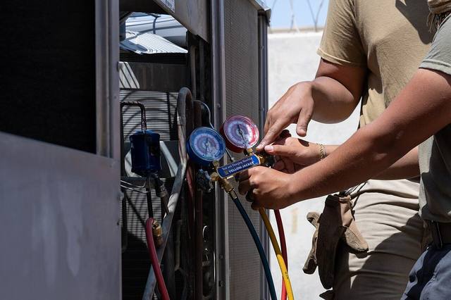 Technician connecting manifold gauges to an outdoor air conditioning unit during a service check in Tulsa