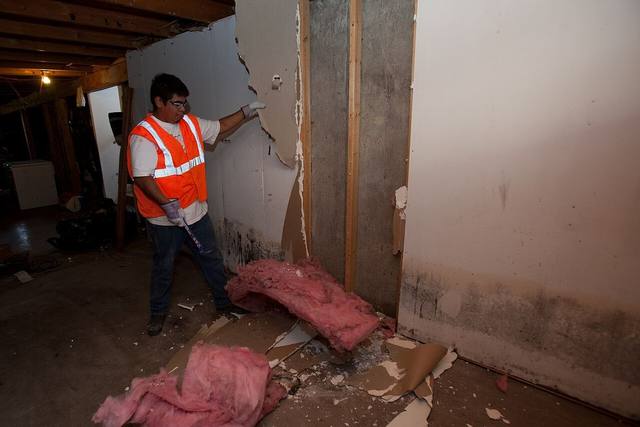 Worker removing water damaged wall material in a basement after a flood loss