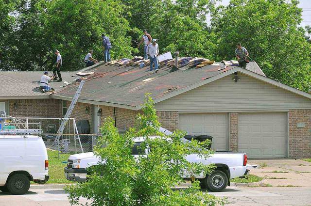 Roofing crew replacing storm-damaged shingles on a brick home, the repair that stops a roof leak at its source
