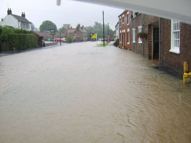 Floodwater covering a residential street between brick homes after heavy rain