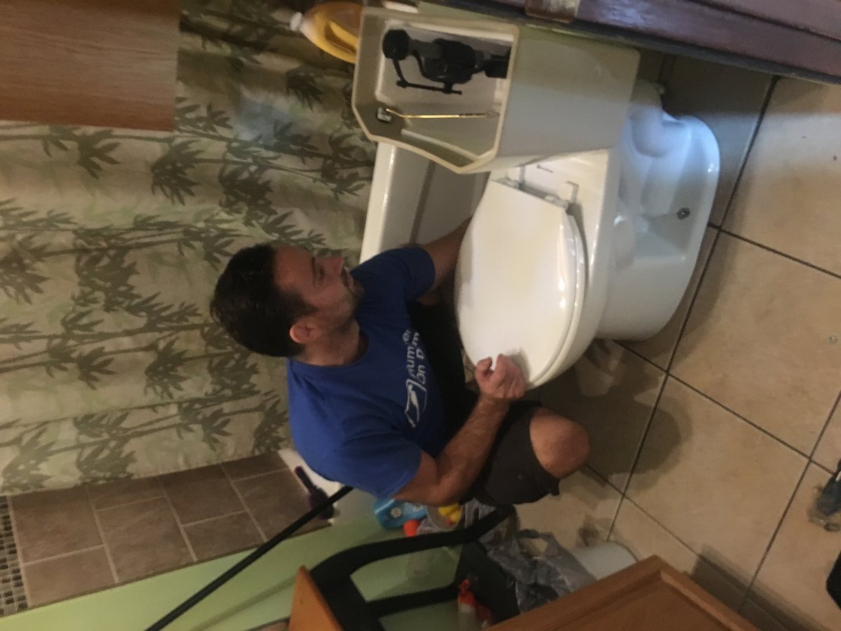 A man kneeling beside a toilet while repairing a leak