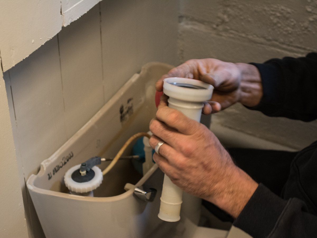 Hands replacing a toilet fill valve inside the tank during an overflow repair