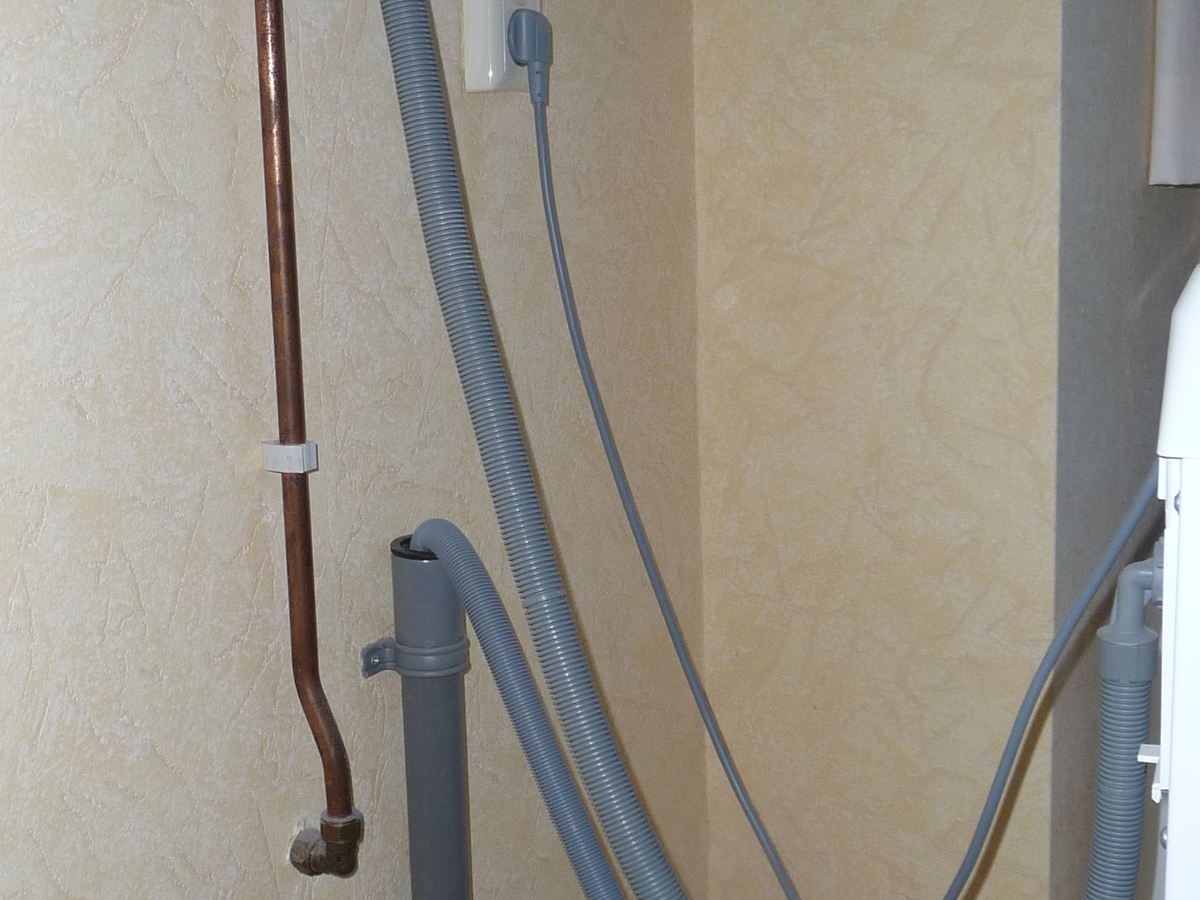Water supply hoses and drain connections behind a washing machine