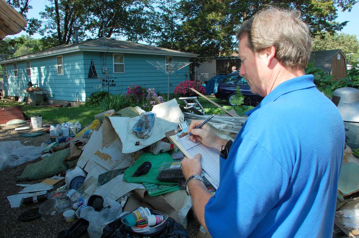 A specialist writing scope notes on a clipboard in front of a flood damaged house