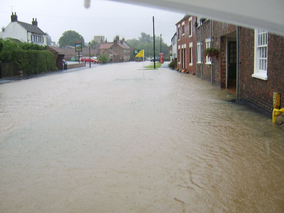 Floodwater covering a residential street between brick homes after heavy rain