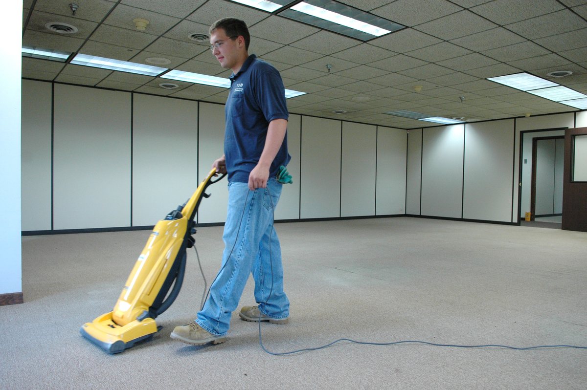 A worker running a carpet extraction machine in an empty office