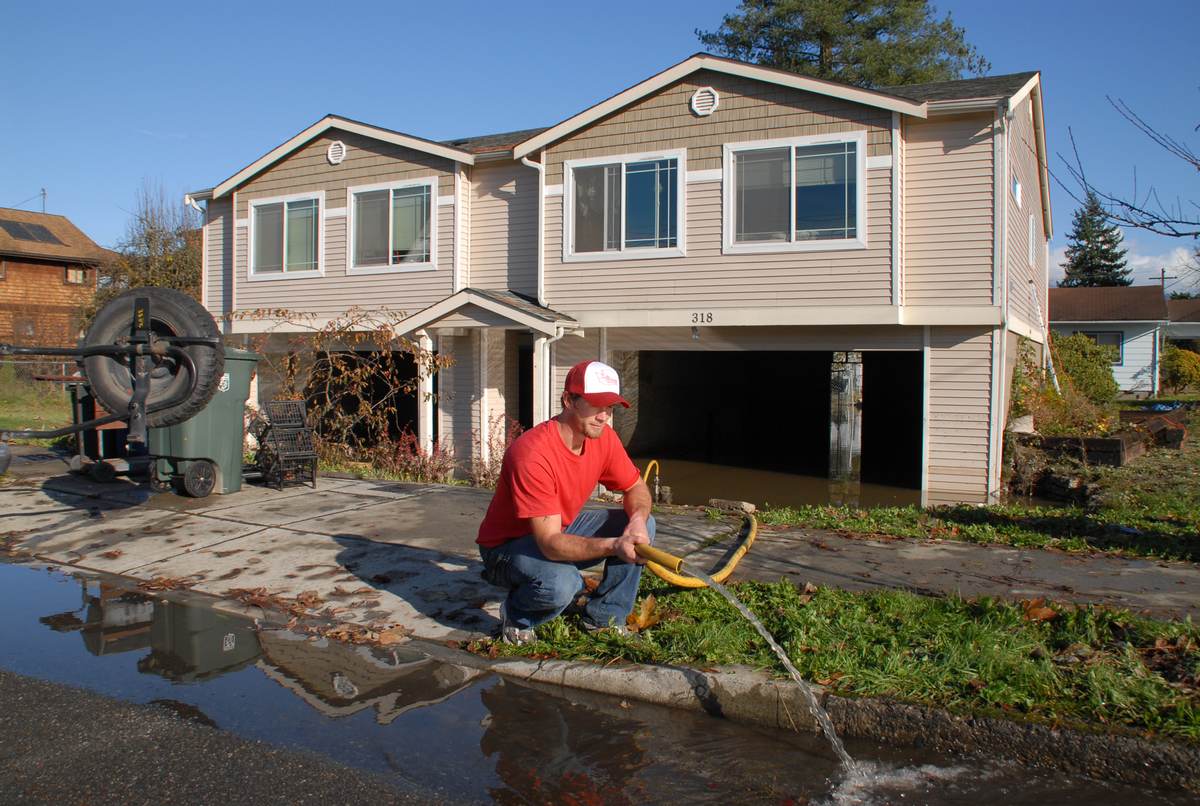 A worker pumping water out of a flooded home with a hose