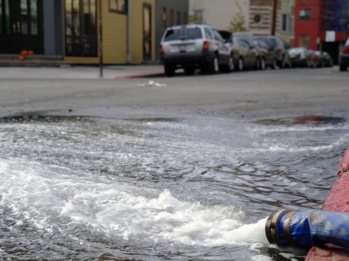 Pump discharge hose pushing floodwater out of a flooded basement onto the street