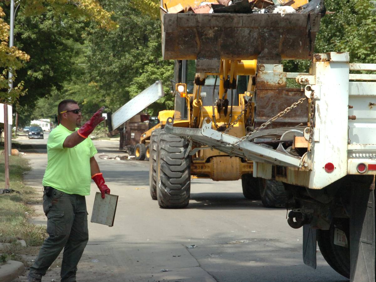 Loader clearing flood debris from a neighborhood street into a dump truck