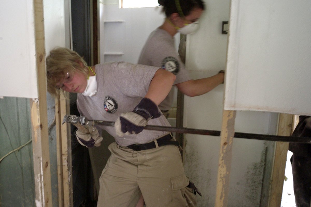 Workers prying out a water damaged wall panel during mitigation